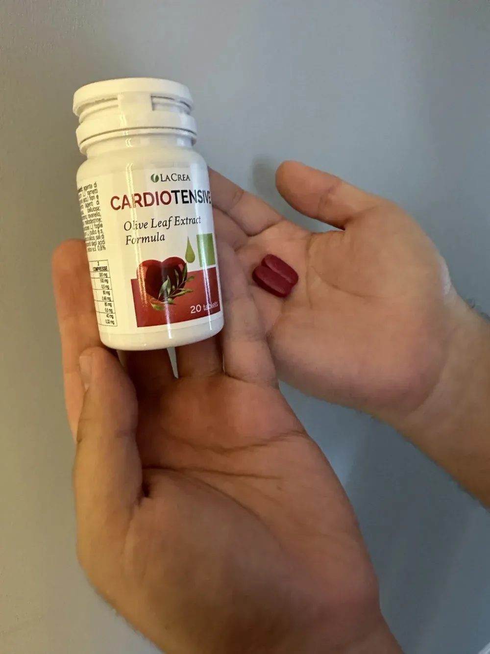 Due compresse di Cardiotensive sul palmo di una mano, accanto al flacone
